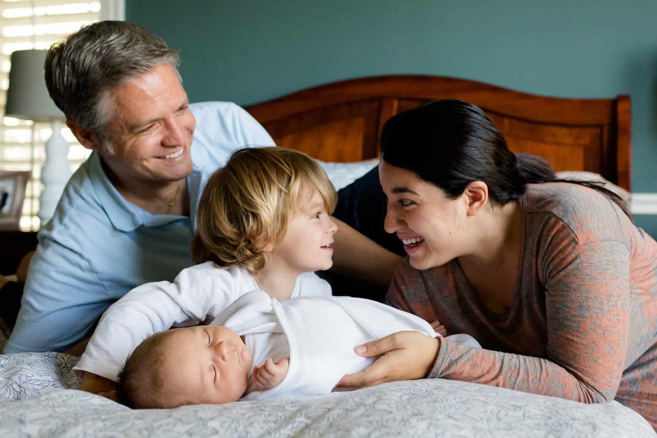 Na zdjęciu widzimy ujęcie rodziny, która spędza czas na łóżku. W centrum uwagi są rodzice ze swoimi dziećmi. To piękne ujęcie zachęca nas do zatrzymania się na chwilę i docenienia prostych, ale cennych momentów spędzonych z najbliższymi